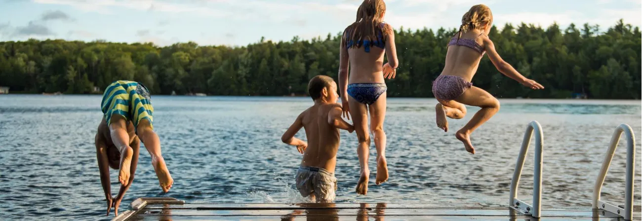 Kinder springen von einem Holzsteg in den See