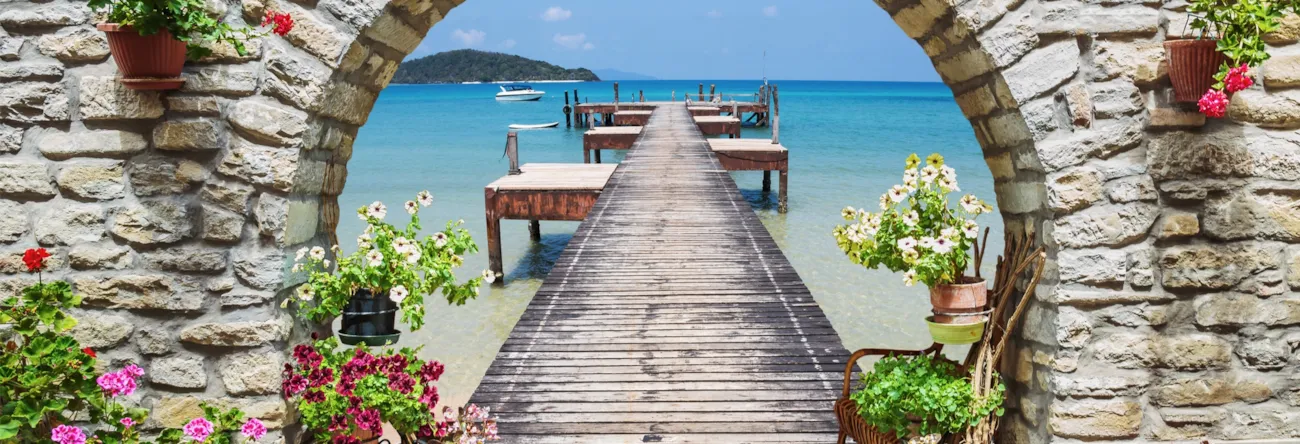 Blick durch Steinbogen auf einen Steg im Meer in Italien