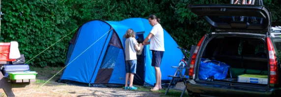 Vater und Sohn stehen neben blauem Zelt und Auto