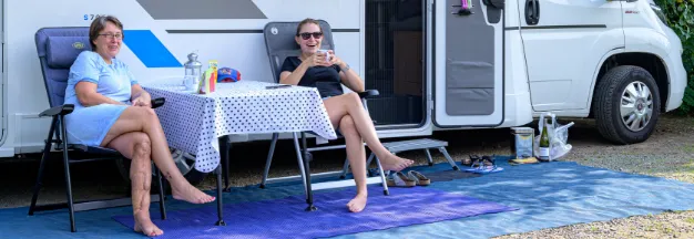 Zwei Frauen sitzen auf Campingstühlen vor ihrem Wohnmobil