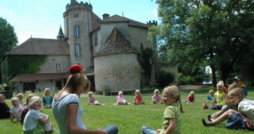 Gruppe Kinder sitzt im Spielkreis auf einer Wiese neben einer Schlossanlage