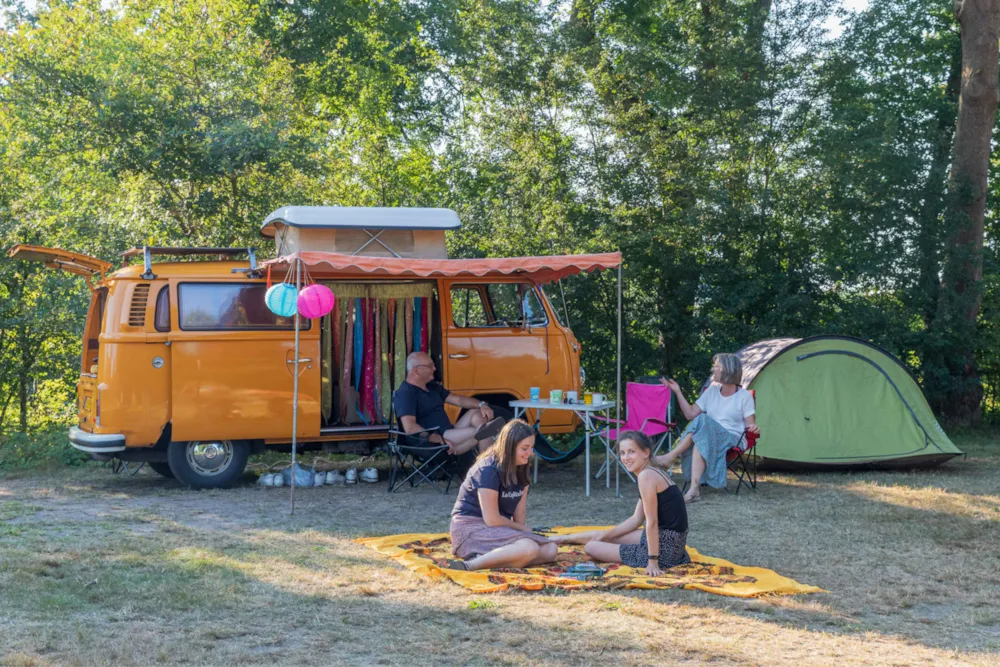 Familie sitzt vor einem gelben Campingwagen und Zelt