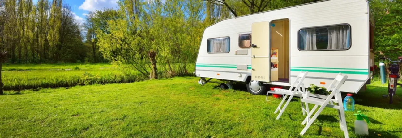 Zwei Klappstühle vor Campingwagen auf grüner Wiese