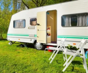 Zwei Klappstühle vor Campingwagen auf grüner Wiese