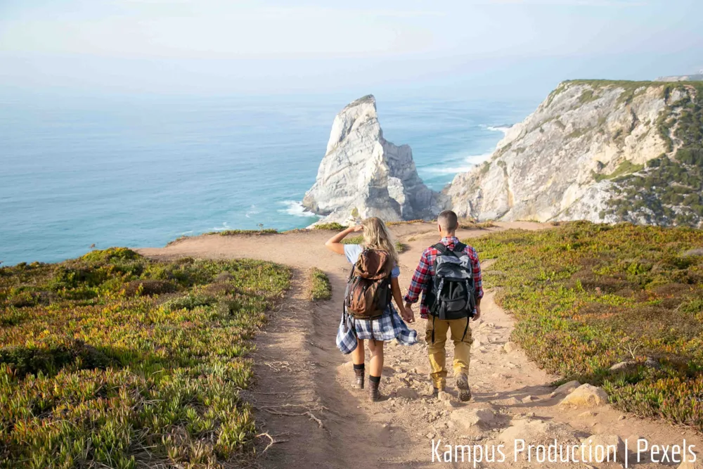 Paar mit Rucksack und Wanderschuhen geht auf Klippen am Meer zu