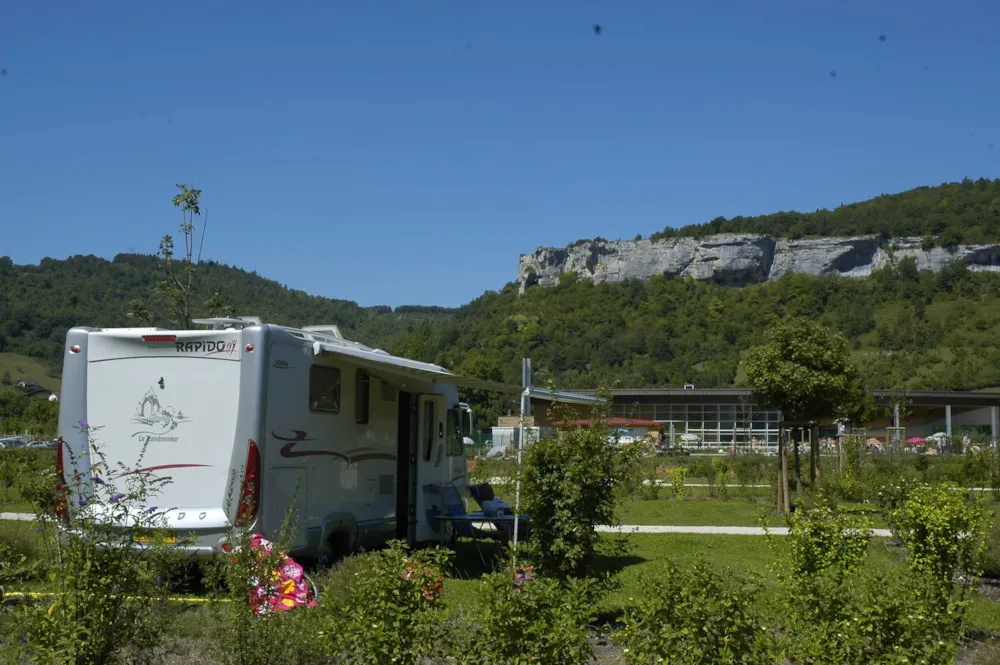 Wohnwagen auf grünem Stellplatz im Hintergrund Bergfels