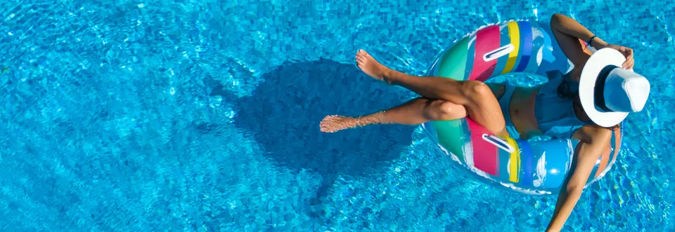 Frau mit Badeanzug und Sonnenhut treibt entspannt auf gestreiftem Schwimmreifen im Pool