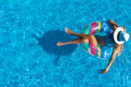 Frau mit Badeanzug und Sonnenhut treibt entspannt auf gestreiftem Schwimmreifen im Pool