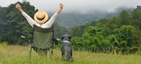 Frau auf Campingstuhl genießt die Natur mit ihrem Hund