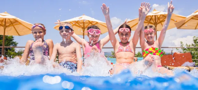 Kinder sitzen auf dem Beckenrand eines Pools auf einem Campingresort