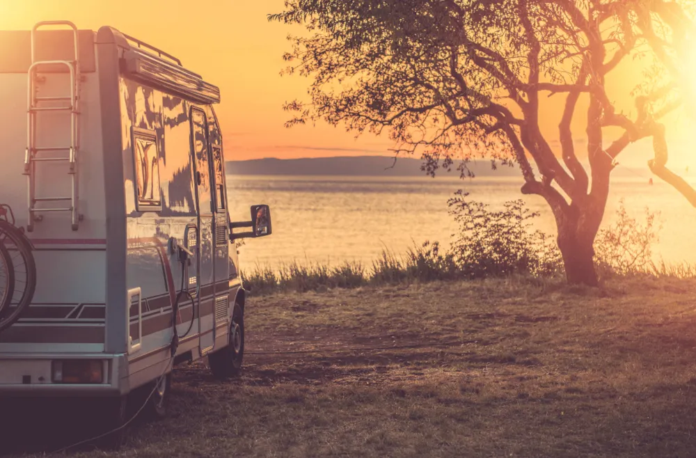 Wohnwagen auf Stellplatz mit Blick aufs Wasser bei herbstlichem Sonnenuntergang