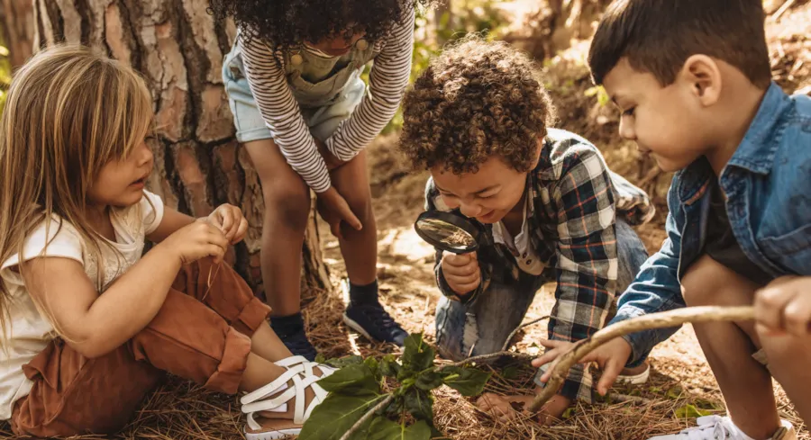 Kleine Kinder spielen in der Natur und untersuchen Erdboden mit Lupe