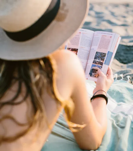 Vacancière consultant un guide de camping sur la plage pendant ses vacances - Naturisme.fr