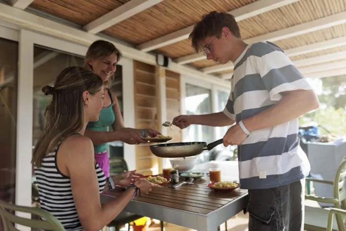 Famille avec adolescents en camping, en train de manger sur la terrasse d'un mobil-home