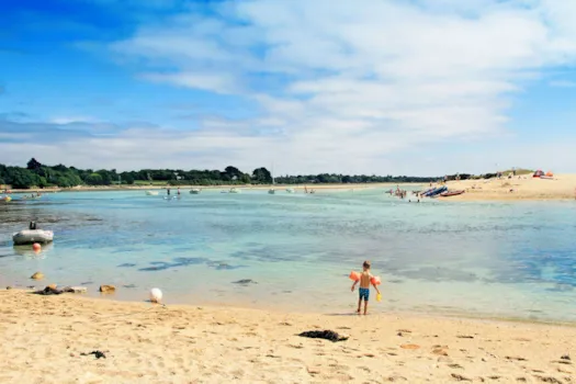 Kleines Kind mit Schwimmflügeln und Eimer steht an einem flachen Strand