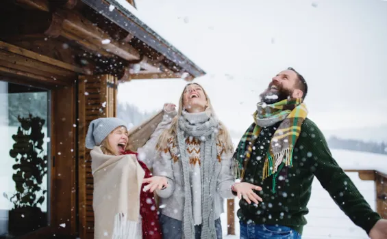 Familie mit kleinem Mädchen, das sich auf der Terrasse im Freien vergnügt, Urlaub in der winterlichen Natur.