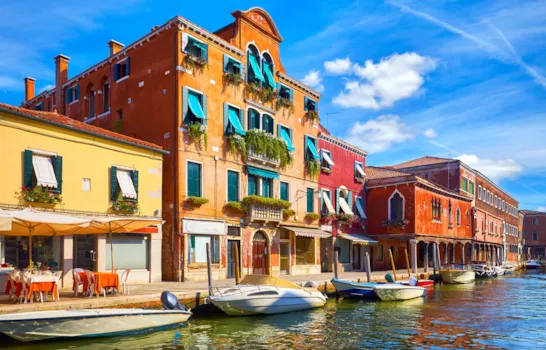 Die Insel Murano in Venedig, Italien. Ein jahrhundertealtes italienisches Haus am Kanal mit Motorbooten. Blauer Himmel und weiße Wolken über Murano. Ein sonniger Sommertag. 