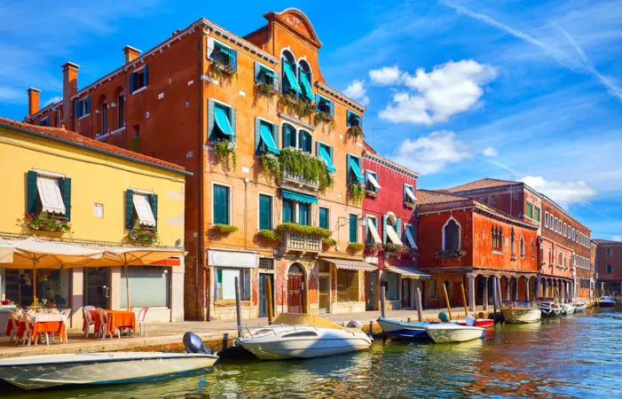 Die Insel Murano in Venedig, Italien. Ein jahrhundertealtes italienisches Haus am Kanal mit Motorbooten. Blauer Himmel und weiße Wolken über Murano. Ein sonniger Sommertag. 