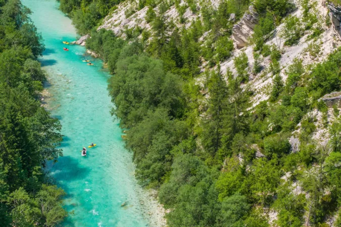 Kajakfahrer erkunden die türkisfarbenen Gewässer des Flusses Soca in einem üppig bewachsenen Tal inmitten einer bergigen Landschaft, Slowenien