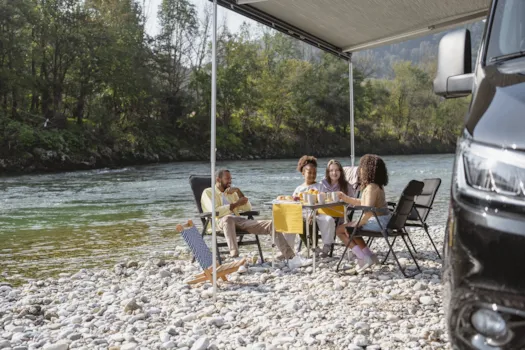 Familie vor ihrem Wohnmobil auf einem kleinen Campingplatz am Flussufer