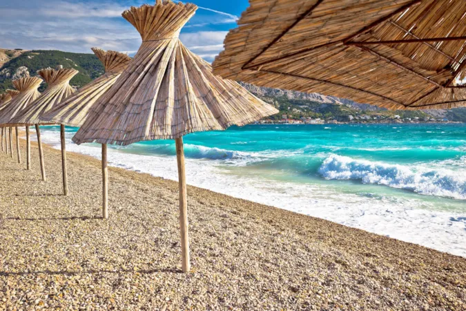 Idyllischer Strand mit Blick auf den Horizont hinter Sonnenschirmen, Baska, Insel Krk, Kroatien
