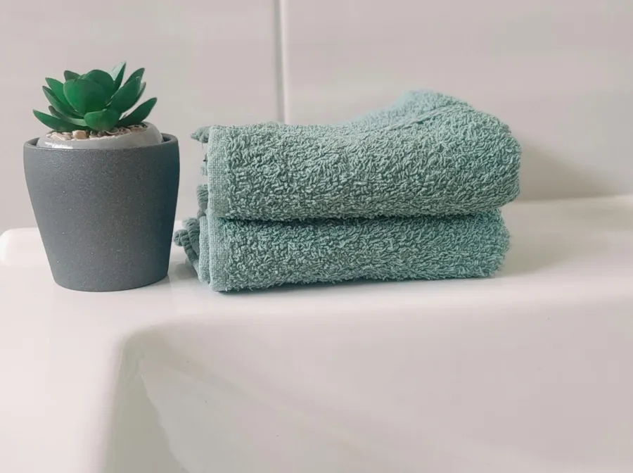 Frische salbeifarbene Handtücher und Topf mit Pflanze an einem Waschbeckenrand