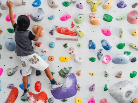 Kind klettert in einer bunten Boulder-Kletterwand