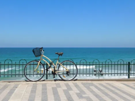 Fahrrad lehnt an Geländer an Strandpromenade; im Hintergrund das blaue Meer