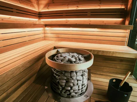 Sauna-Aufgusskübel mit Kohlen, im Hintergrund beleuchtete Holzbank in Sauna