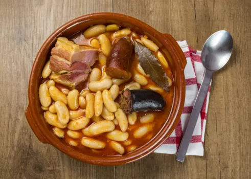 Draufsicht auf Tapasteller mit karierter Serviette und Löffel: Fabada asturiana, die vor allem in der Nebensaison in Spanien angeboten werden
