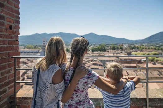 Eine Familie besucht Lucca in der Toskana: Mutter mit zwei Kindern in Rückenansicht, die von einem der Türme auf die Stadt blicken