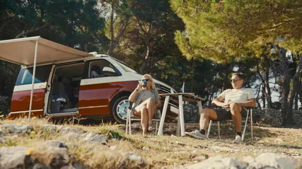 Ein glückliches Paar mittleren Alters genießt seinen Kaffee auf Campingstühlen vor seinem Wohnmobil auf einem XL-Stellplatz.
