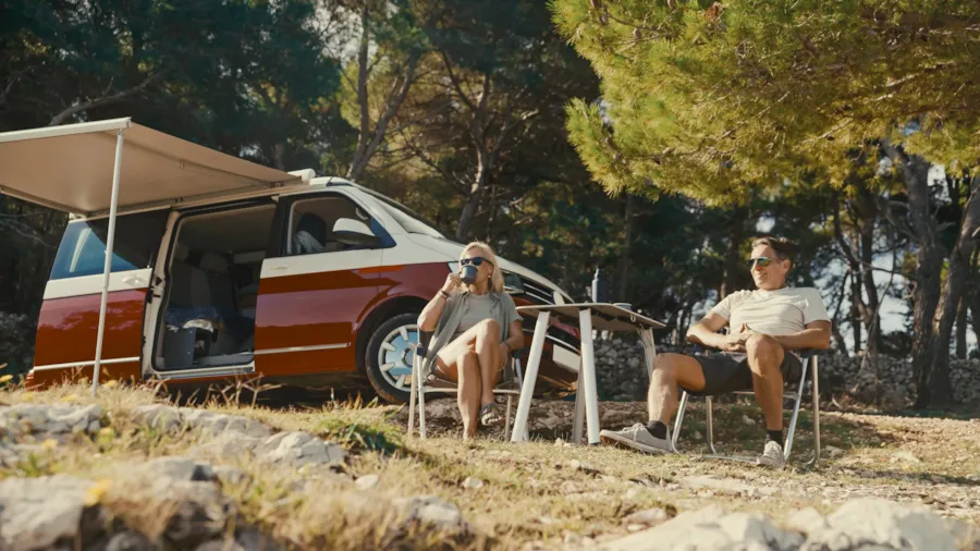 Ein glückliches Paar mittleren Alters genießt seinen Kaffee auf Campingstühlen vor seinem Wohnmobil auf einem XL-Stellplatz.