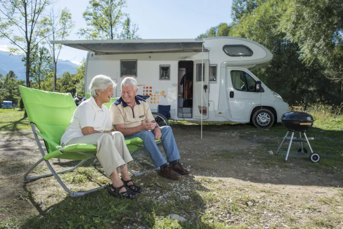 Ein Senioren-Paar sitzt auf Campingstühlen vor seinem Wohnmobil auf einem XL-Stellplatz.