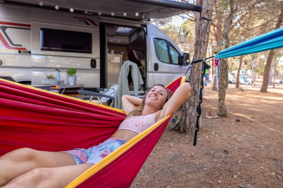 Eine junge Frau entspannt in einer Hängematte neben einem Wohnmobil auf einem XL-Stellplatz.