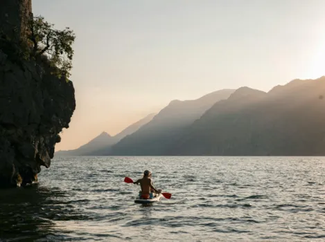 Jugendliche auf Stand up Paddle rund um die Felsen von Malcesine am Gardasee bei Abendsonne