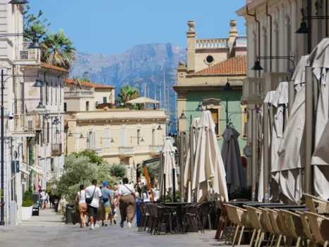 Charmante Straße mit historischen Gebäuden, eingeklappten Sonnenschirmen vor den Cafés und spazierenden Touristen in Olbia, Sardinien, Italien