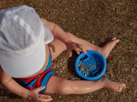 Blick von oben auf Baby am Strand mit Sandsieb