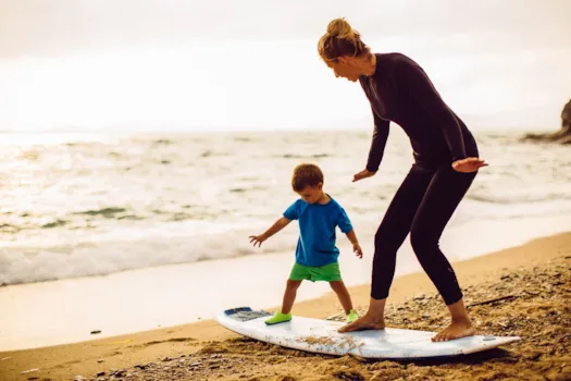 Frau und kleiner Junge machen Übungen auf einem Surfbrett am Strand 