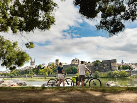 Zwei Radfahrer blicken auf das Château d’Angers am Flussufer in Frankreich.