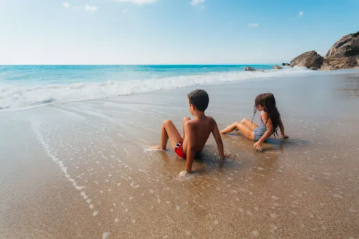 Kleines Mädchen und kleiner Junge sitzen am Strand im seichten Wasser der auslaufenden Wellen