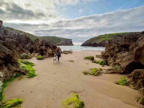 Frau mit Hund an einem einsamen Strand bei Llanes an der asturischen Küste
