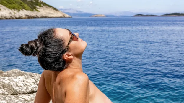 Nackte Frau sonnt sich am Meer an einer felsigen Küste