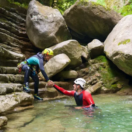 Frau hilft Mann aus dem Wasser beim Canyoning