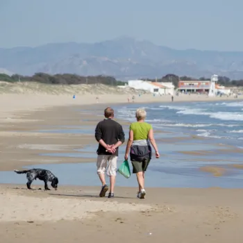 Ein älteres Paar geht mit seinem Hund am Strand von La Marina in Alicante, Spanien, spazieren