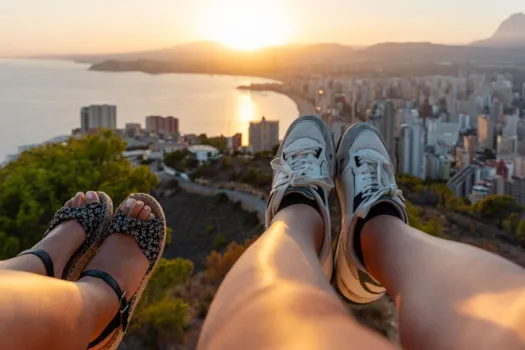 Paar lässt seine Beine baumeln über der  Stadtlandschaft von Benidorm bei Sonnenuntergang, Spanien