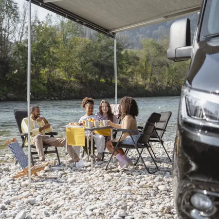 Familie vor ihrem Wohnmobil auf einem kleinen Campingplatz am Flussufer