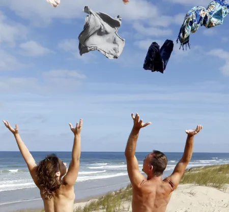 Deux vacanciers lançant leurs vêtements en l'air sur une plage - Naturisme.fr