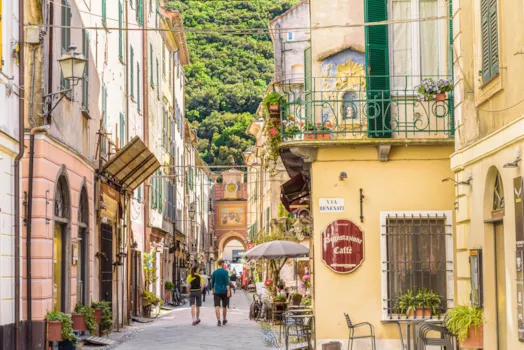 Finalborgo, Finale Ligure, Italien. Blick von der Porta Testa auf den Uhrturm in der engen Via Giovanni Nicotera. Einige Touristen spazieren durch die Straße.