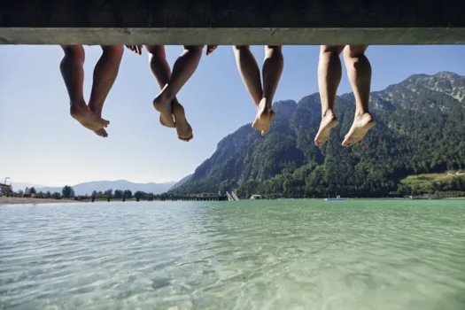 Familie sitzt mit den Füßen über dem Wasser an einem See vor einer Bergkulisse in den österreichischen Alpen.